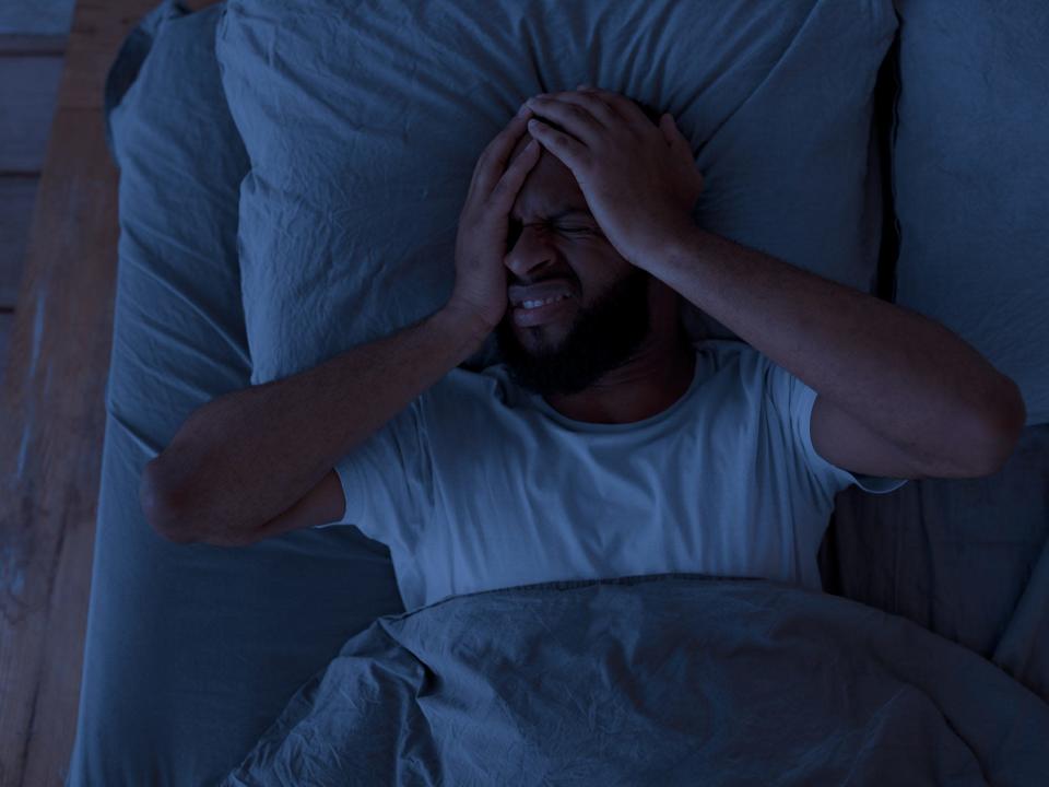 A man awake in bed at night holding his head in both hands, suffering from insomnia or headache
