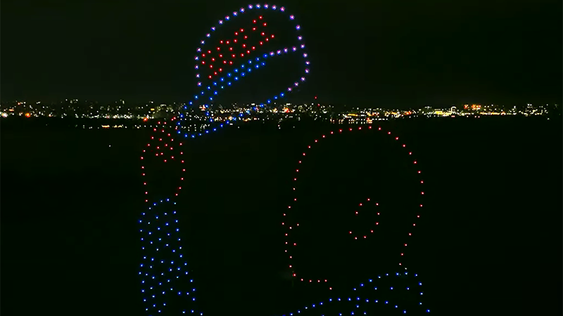 Drones taking the shape of a man holding a hat reading "2020" in front of the New York City skyline.