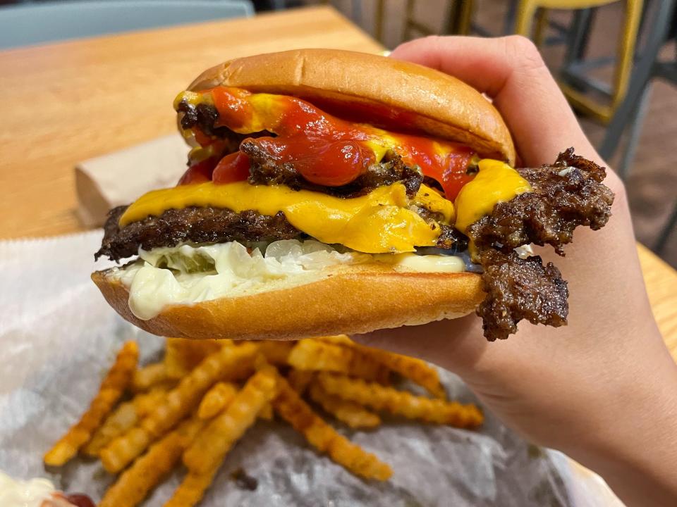 A hand holding a burger  near fries