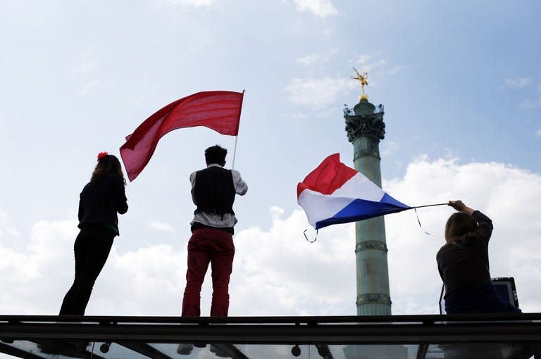 Protesters hold a France's national flag (R) and a red flag, on May 5, 2013 on the Bastille square in Paris, as they take part in a demonstration. Tens of thousands of protesters took to the streets of Paris on Sunday to mark Socialist President Francois Hollande's first year in office by accusing him of turning his back on the left