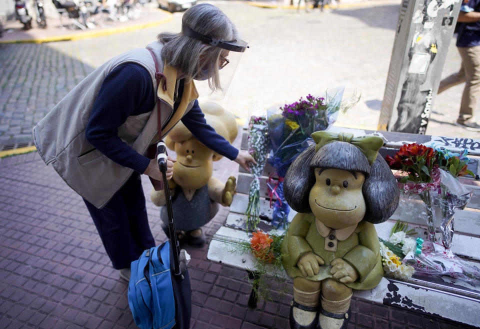 A woman places a flower bouquet next to statue of the comic strip character Mafalda created by Argentine cartoonist Joaquin Salvador Lavado, who was better known as Quino, in Buenos Aires, Argentina, Wednesday, Sept. 30, 2020. Lavado passed away on Wednesday, according to his editor Daniel Divinsky who announced it on social media. He was 88. (AP Photo/Victor R. Caivano)