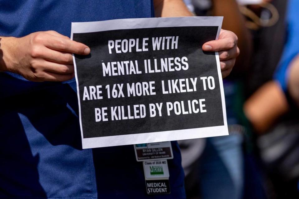 University of Miami Medical Student Ryan Gillen holds a sign that reads “People With Mental Illness Are 16x More Likely To Be Killed By Police” during a press conference held by the Healing and Justice Center across the street from the scene of the shooting at NW 58th St and NW 7th Court, in Liberty City, Florida, on Thursday, March 14, 2024. City of Miami police officers shot Donald Armstrong last week more than five times while responding to an emergency call during a mental health crisis.