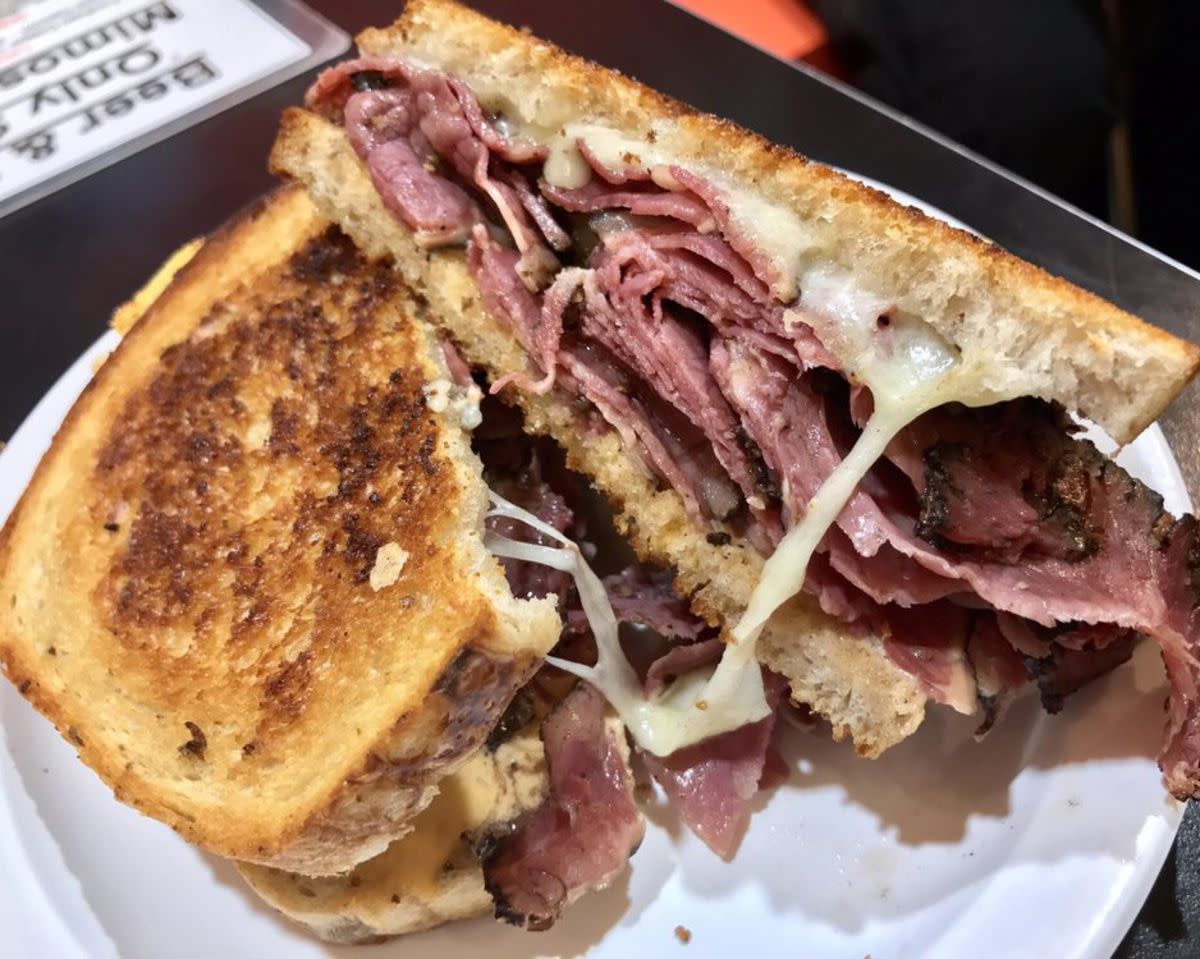 Closeup of Colossal Reuben on a white paper plate, Chick & Ruth's Delly, Annapolis, Maryland, a menu is blurred in the top left background