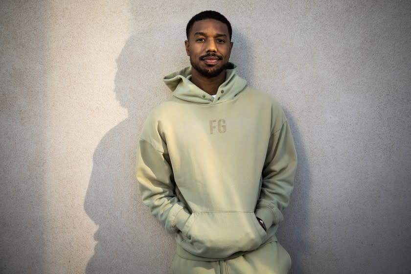 A man leaning against a white wall in a green hoodie