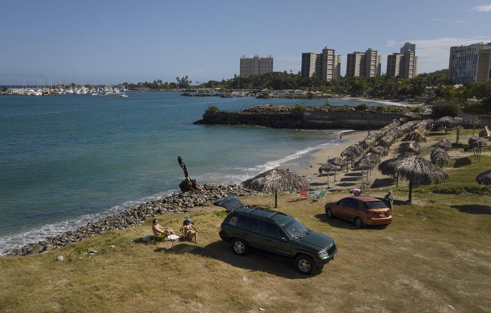 Couple Juan Peñalver and Victoria Colina rest on Mansa beach after it recently reopened following a lockdown to contain the spread of COVID-19 in La Guaira, Venezuela, Friday, Oct. 23, 2020. Strict quarantine restrictions forced the closure of beaches across the country in March and reopened this week in hopes of revitalizing the battered economy. (AP Photo/Matias Delacroix)