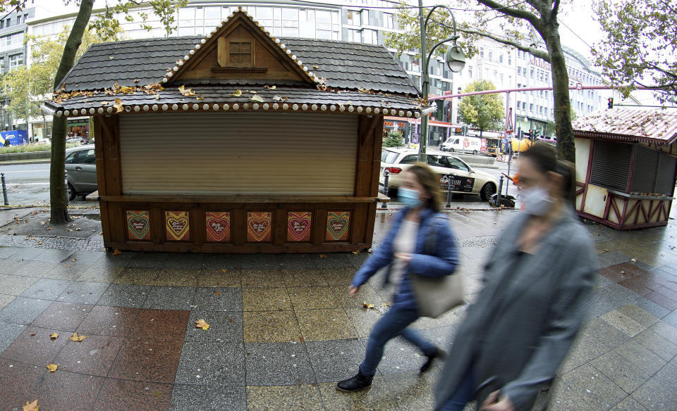 FILE - In this Monday, Nov. 2, 2020 file photo, two woman walk past closed Christmas market booths on a famous shopping road close to the Kaiser Wilhelm Memorial Church in Berlin, Germany. Nations are struggling to reconcile cold medical advice with a holiday tradition that calls for big gatherings in often poorly ventilated rooms, where people chat, shout and sing together, providing an ideal conduit for a virus that has killed over 350,000 people in Europe so far. (AP Photo/Michael Sohn, File)