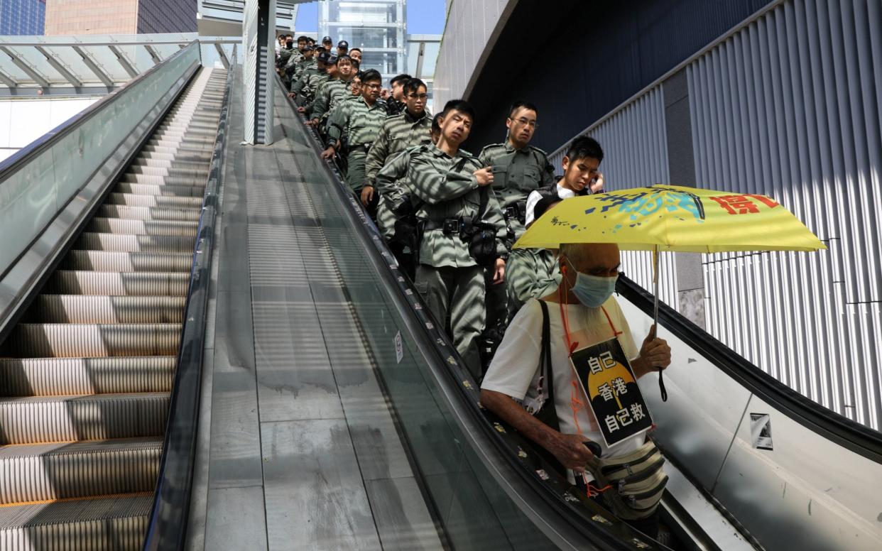 A line of police officers ride an escalator behind a protester holding an umbrella - REUTERS