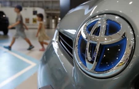 Visitors walk past a logo of Toyota Motor Corp on a Toyota Prius hybrid vehicle at the company's showroom in Tokyo August 5, 2014. REUTERS/Yuya Shino