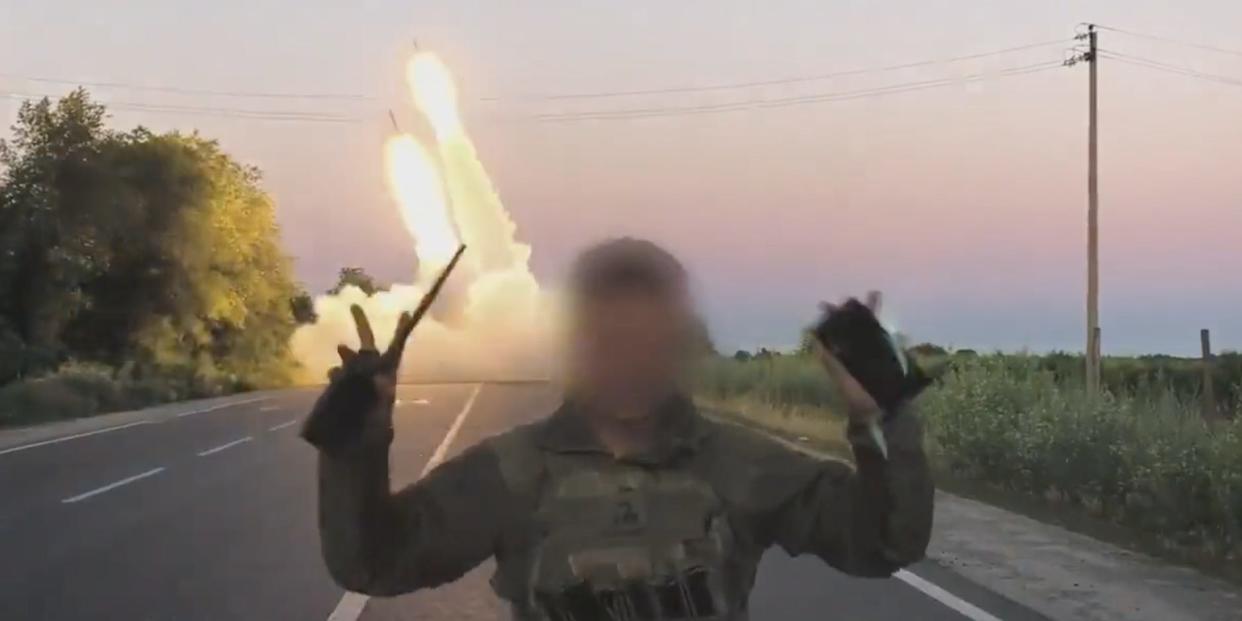 A still from footage shared by the Ukrainian Defense Ministry shows a soldier, whose face is obscured, raise his hands in a "v for victory" as a US-donated HIMARS system launches rockets in the background.