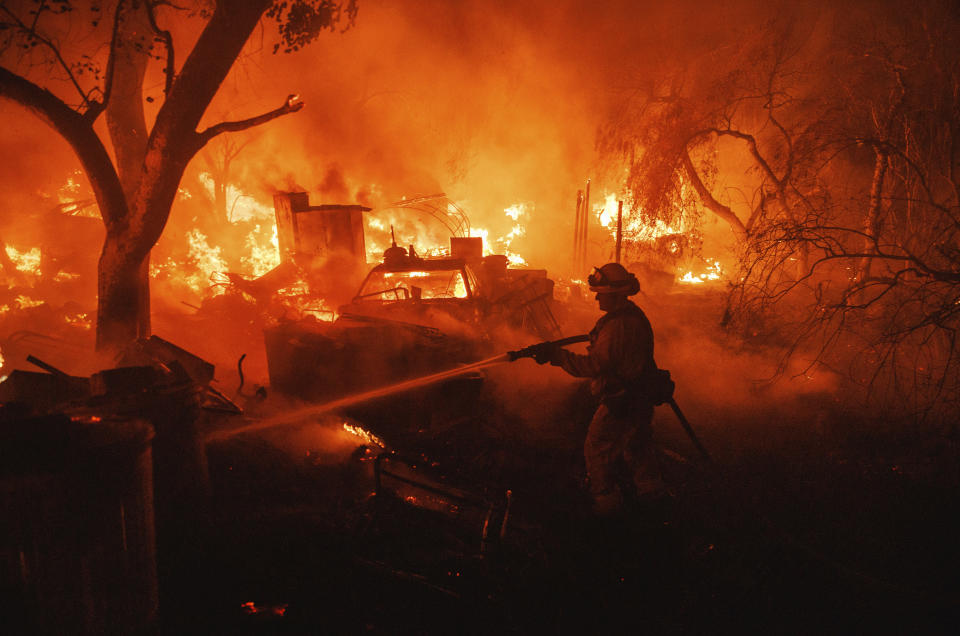 A firefighter takes a hose to a burning property while battling the Fairview Fire Monday, Sept. 5, 2022, near Hemet, Calif. (AP Photo/Ethan Swope)