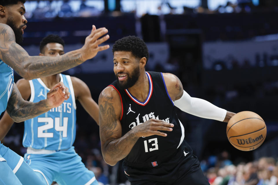Los Angeles Clippers forward Paul George (13) drives into Charlotte Hornets center Nick Richards, left, as forward Brandon Miller looks on during the first half of an NBA basketball game in Charlotte, N.C., Sunday, March 31, 2024. (AP Photo/Nell Redmond)