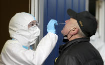 A medical worker, left, tests a man for COVID-19 in a set up for rapid new coronavirus testing in Vienna, Austria, Monday, Nov. 30, 2020. The Austrian government has moved to restrict freedom of movement for people, in an effort to slow the onset of the COVID-19 disease and the spread of the coronavirus. (AP Photo/Ronald Zak)