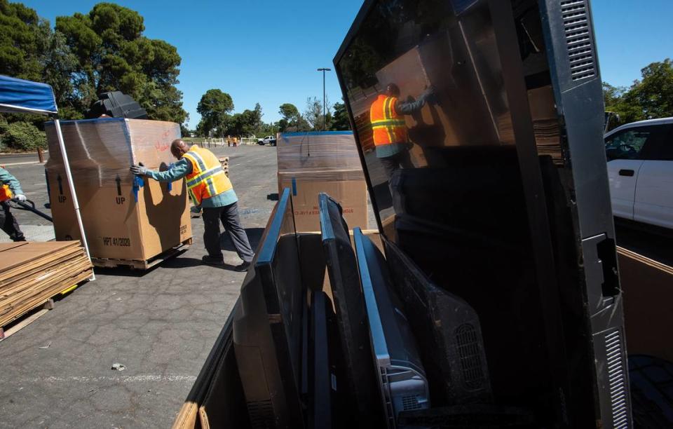 Onsite Electronic Recycling workers Damion Bessard, middle, and Rolando Ibarra wheel a crate full of CRT monitors and televisions during a Modesto city sponsored trash day at John Thurman Field in Modesto, Calif., on Saturday, June, 25, 2022.