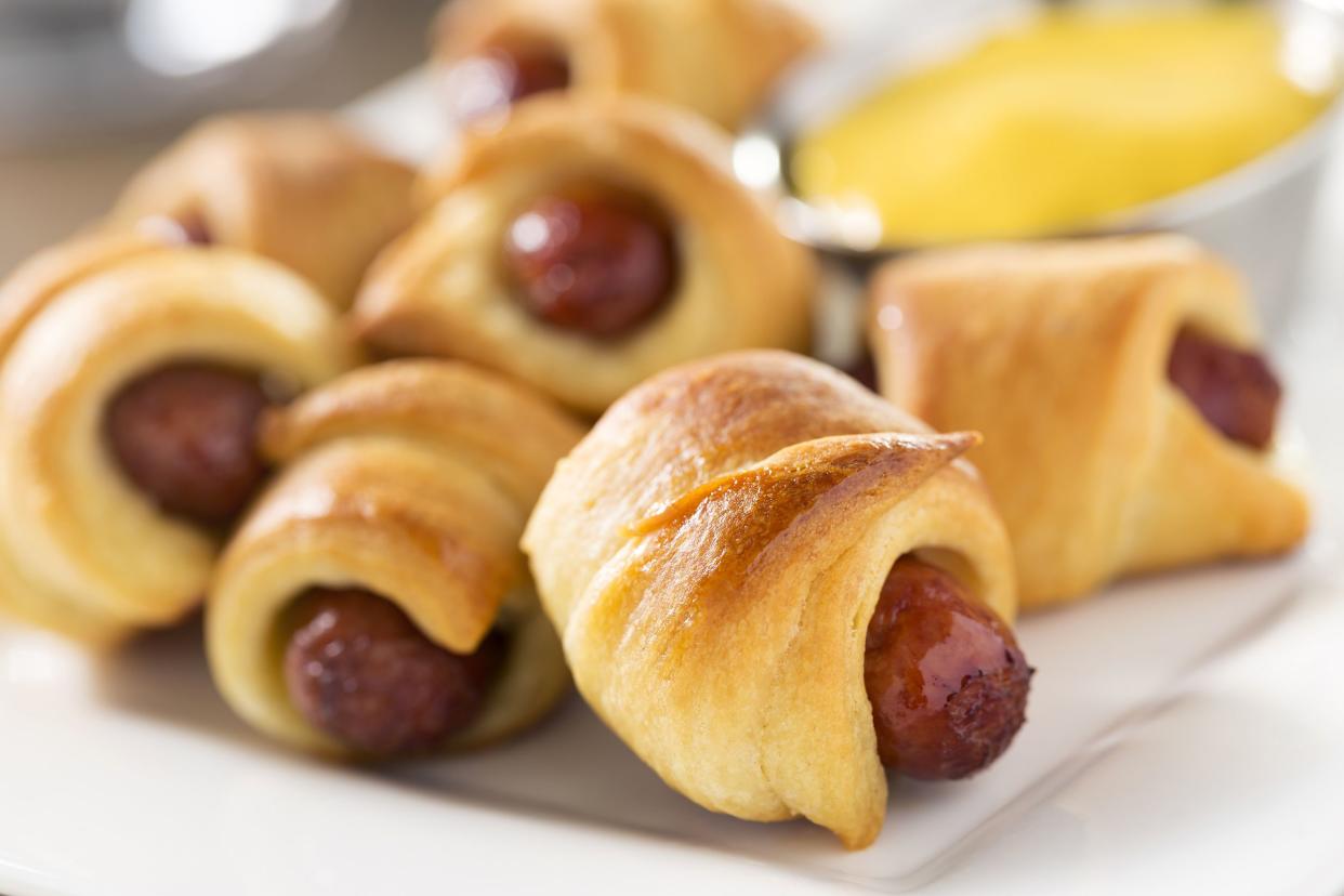 Closeup of pigs in a blanket on a white square plate with a blurred background