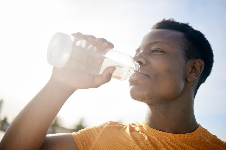 Person wearing a casual shirt, drinking water from a bottle outside on a sunny day