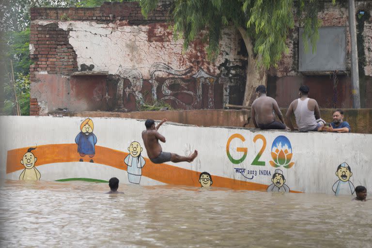 Residentes de las orillas del río Yamuna están sentados junto a una calle inundada en Nueva Delhi, India, jueves 13 de julio de 2023. Las inundaciones obligaron a evacuar a miles de personas en las zonas bajas de la capital. 