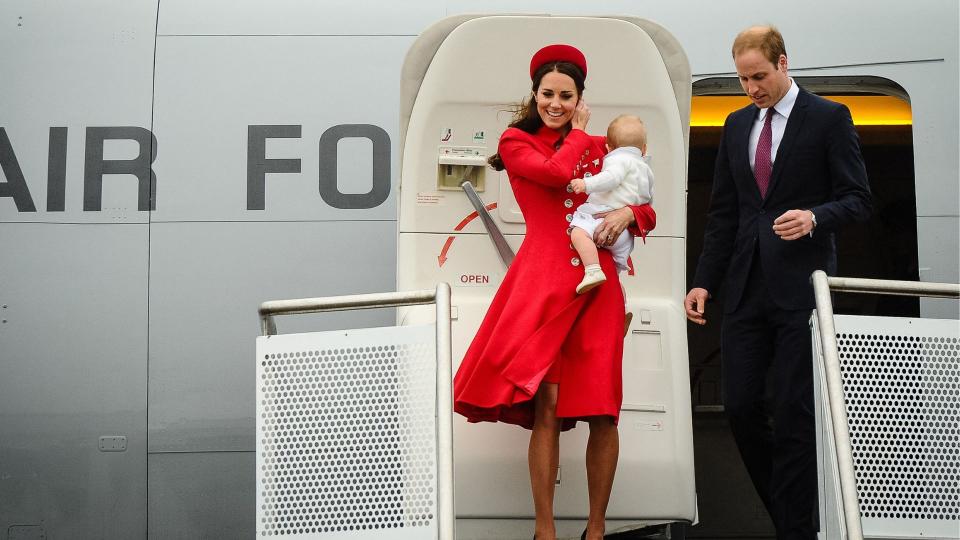 Kate Middleton, Prince William and a baby Prince George exiting a plan on a windy day