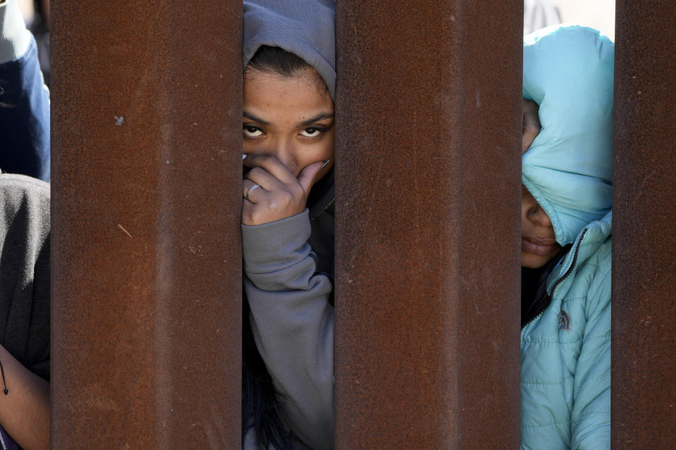 Dos migrantes que aguardan para solicitar asilo entre dos muros fronterizos miran a través de uno de ellos, el jueves 11 de mayo de 2023, en San Diego. Las restricciones estadounidenses al asilo, implementadas por la pandemia de COVID-19 y conocidas como Título 42, expiraron el 11 de mayo. (AP Foto/Gregory Bull)