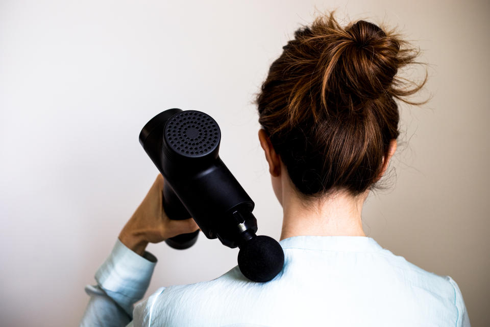 woman using a massage gun on her shoulders