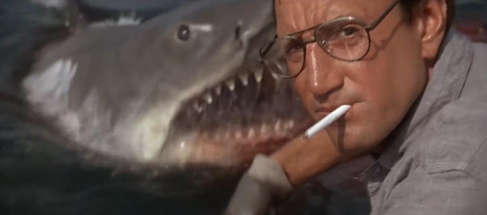 Brody smoking a cigarette with the shark behind him in "Jaws"