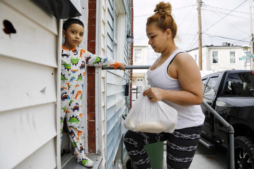 Roberto, 5, stands in their doorway in his pajama's as his mother Arely carries in a bag of food brought to their rental in Baltimore by her sister Janeth, Tuesday, April 14, 2020. Since this image was taken Arely, Janeth, and Janeth's husband Roberto have all been diagnosed with COVID-19, leaving them unable to leave their homes to look for food. Arely was briefly hospitalized with breathing problems as a result of her illness. (AP Photo/Jacquelyn Martin)