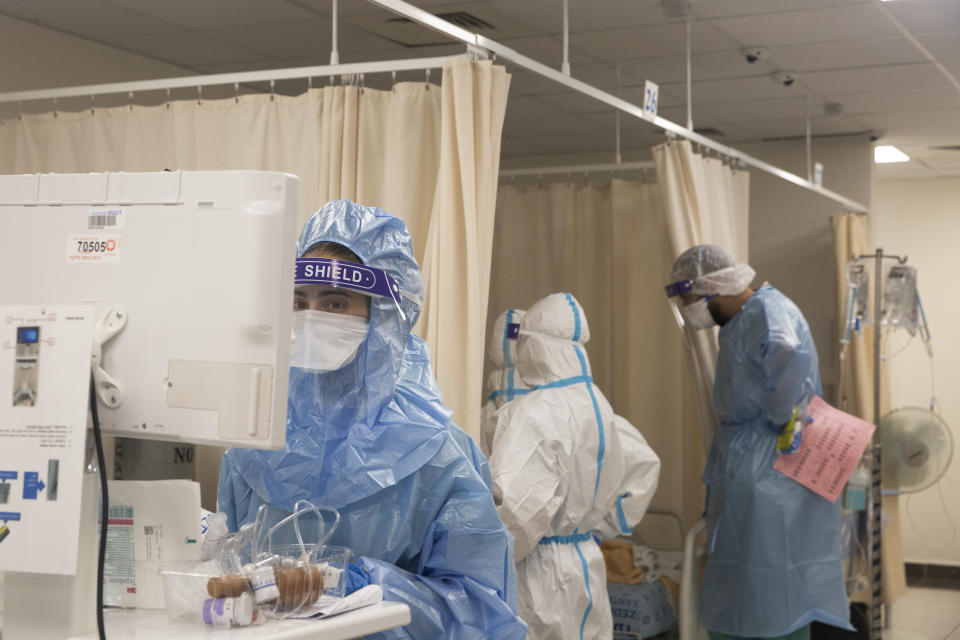 Medical professionals in protective equipment work in the coronavirus ward at Shaare Zedek Medical Center in Jerusalem, Tuesday, Aug. 31, 2021. At left, a medical professional updates a patient's chart in the hospital's computer system as her colleagues speak to a patient behind the curtain at right. (AP Photo/Maya Alleruzzo)