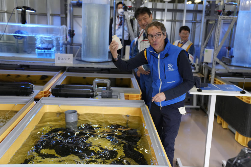 Rafael Mariano Grossi, Director General of the International Atomic Energy Agency, shows off an empty bottle after he fed flounder in a fish tank filled with treated wastewater at a lab, while visiting the damaged Fukushima nuclear power plant in Okuma, northeastern Japan, Wednesday, July 5, 2023. Behind him is Tokyo Electric Power Co. President Tomoaki Kobayakawa. (AP Photo/Hiro Komae, Pool)