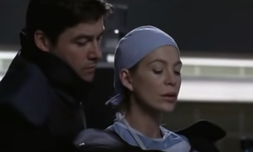 Dylan behind Meredith as she holds the bomb in the patient's chest