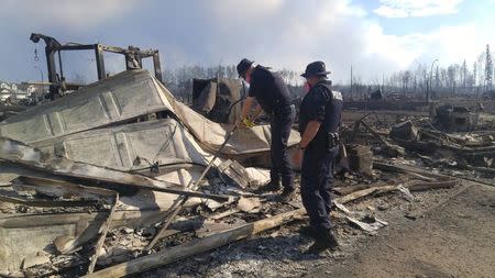 Two Royal Canadian Mounted Police (RCMP) officers survey damage from the large wildfire that is burning in and around Ft McMurray, Alberta, Canada, May 7, 2016. Picture taken May 7, 2016. REUTERS/RCMP/Handout via Reuters