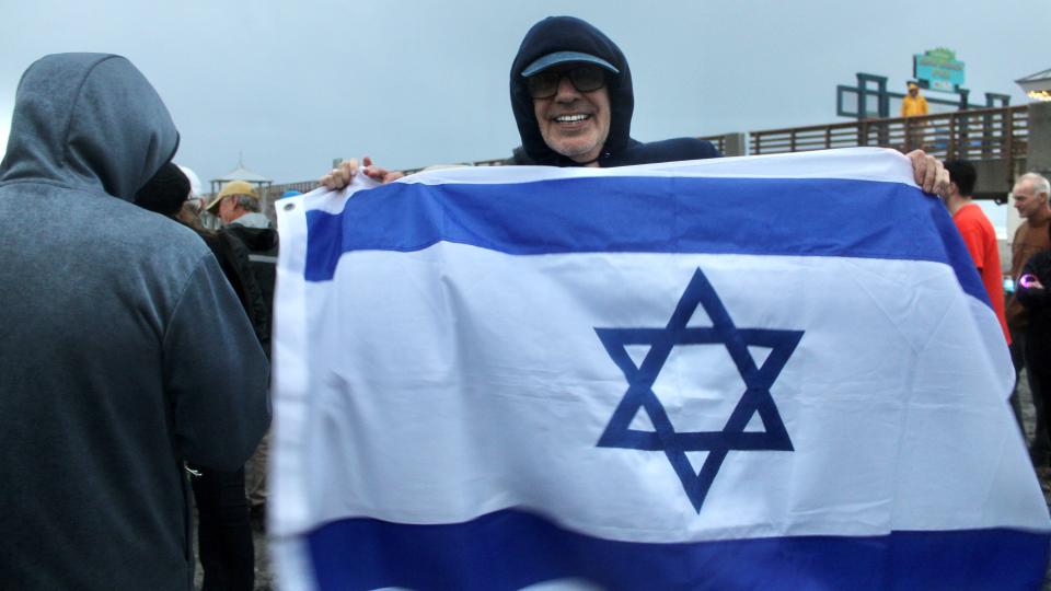 Ira Jacobson of Jupiter, a member of Jewish Community Synagogue of North Palm Beach and the leader of the nonprofit Herut, holds an Israeli flag at a ceremony on Dec. 13, 2023, to relight a sand-sculpture menorah in Juno Beach that vandals had destroyed a day earlier.