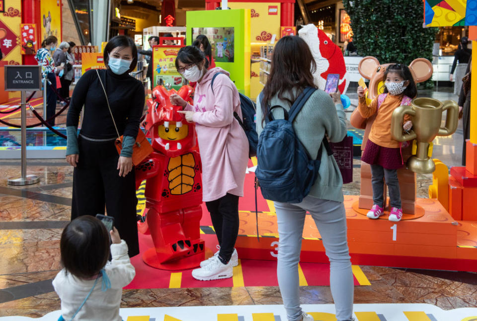 People cover their faces with sanitary masks as they take photos at a shopping mall after the first cases of coronavirus from Wuhan, China were confirmed in Hong Kong. | Miguel Candela–SOPA Images/LightRocket/Getty Images