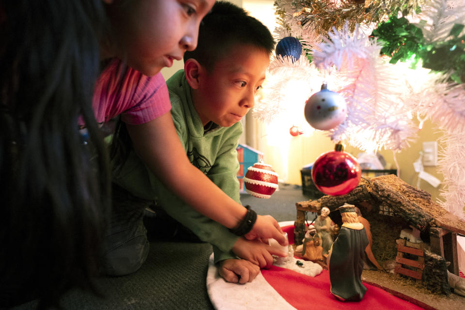 Carolina Mateo Simon, 8, left, and her brother Francisco Mateo Simon, 7, look at a nativity scene under the family's new Christmas tree at their home, Friday, Dec. 15, 2023, in Fort Morgan, Colo. The kids, who were born in Guatemala, had never had a brand-new Christmas tree. Their mother, Magdalena Simon, said the family has had a tree they bought at a second-hand store, but were very happy to have a new tree this year. (AP Photo/Julio Cortez)