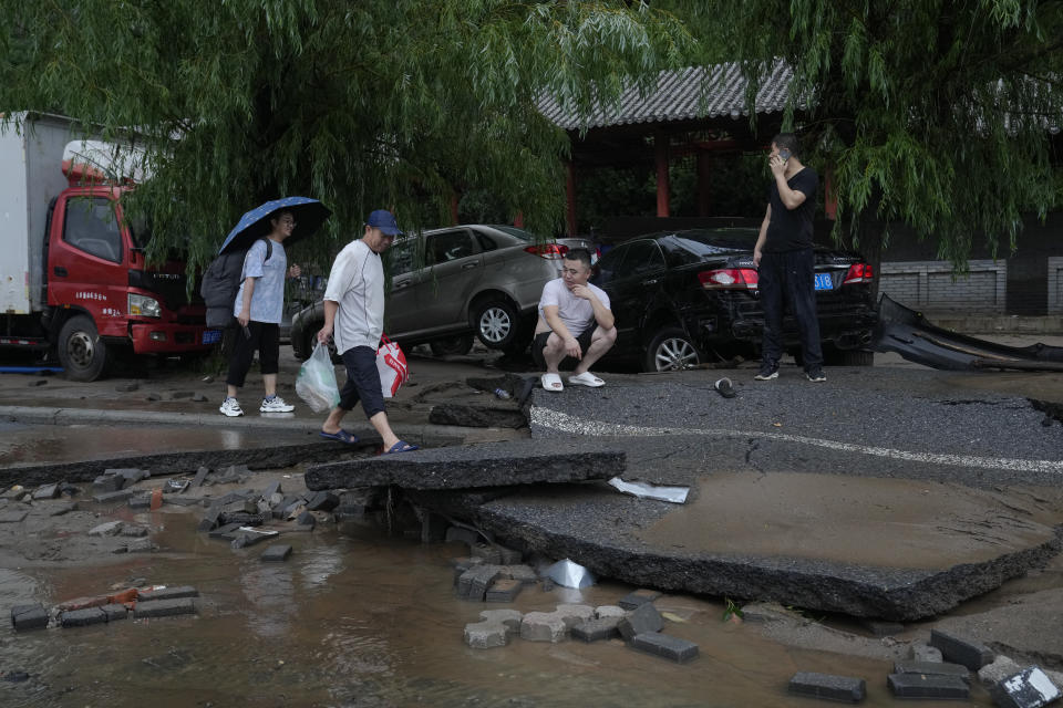 People walk along a damaged road and vehicles swept by flood water in the Mentougou District as continuous rainfall triggers alerts in Beijing, Monday, July 31, 2023. (AP Photo/Andy Wong)