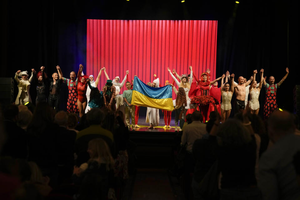 Performers stand on stage with the Ukrainian flag, held by two of their children, at the end of the show "Alice in Wonderland" in Pistoia, Italy, Friday, May 6, 2022. A Ukrainian circus troupe is performing a never-ending “Alice in Wonderland” tour of Italy. They are caught in the real-world rabbit hole of having to create joyful performances on stage while their families at home are living through war. The tour of the Theatre Circus Elysium of Kyiv was originally scheduled to end in mid-March. (AP Photo/Alessandra Tarantino)