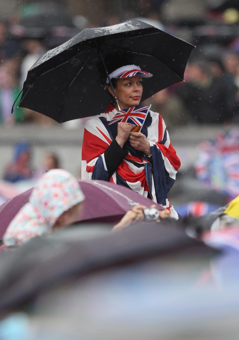 A reveller holds an umbrella in Trafalgar Square as she watches a large screen television monitor showing the Queen and the Royal Family on the balcony of Buckingham Palace.