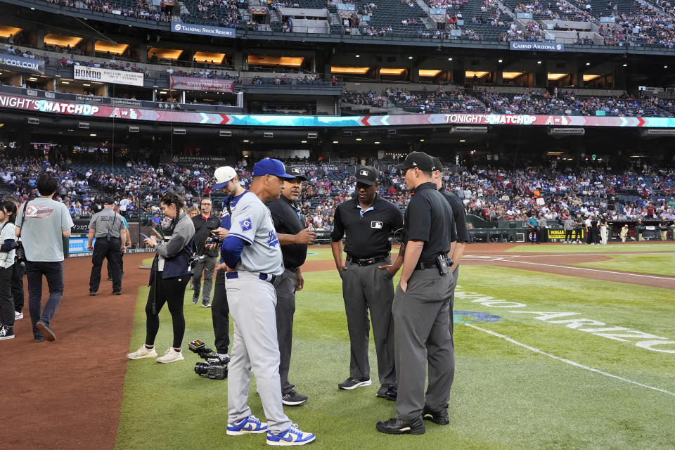 Los Angeles Dodgers manager Dave Roberts, left, talks with the umpires regarding a swarm of bees gathered on the net behind home plate delaying the start of a baseball game against the Arizona Diamondbacks, Tuesday, April 30, 2024, in Phoenix. (AP Photo/Matt York)