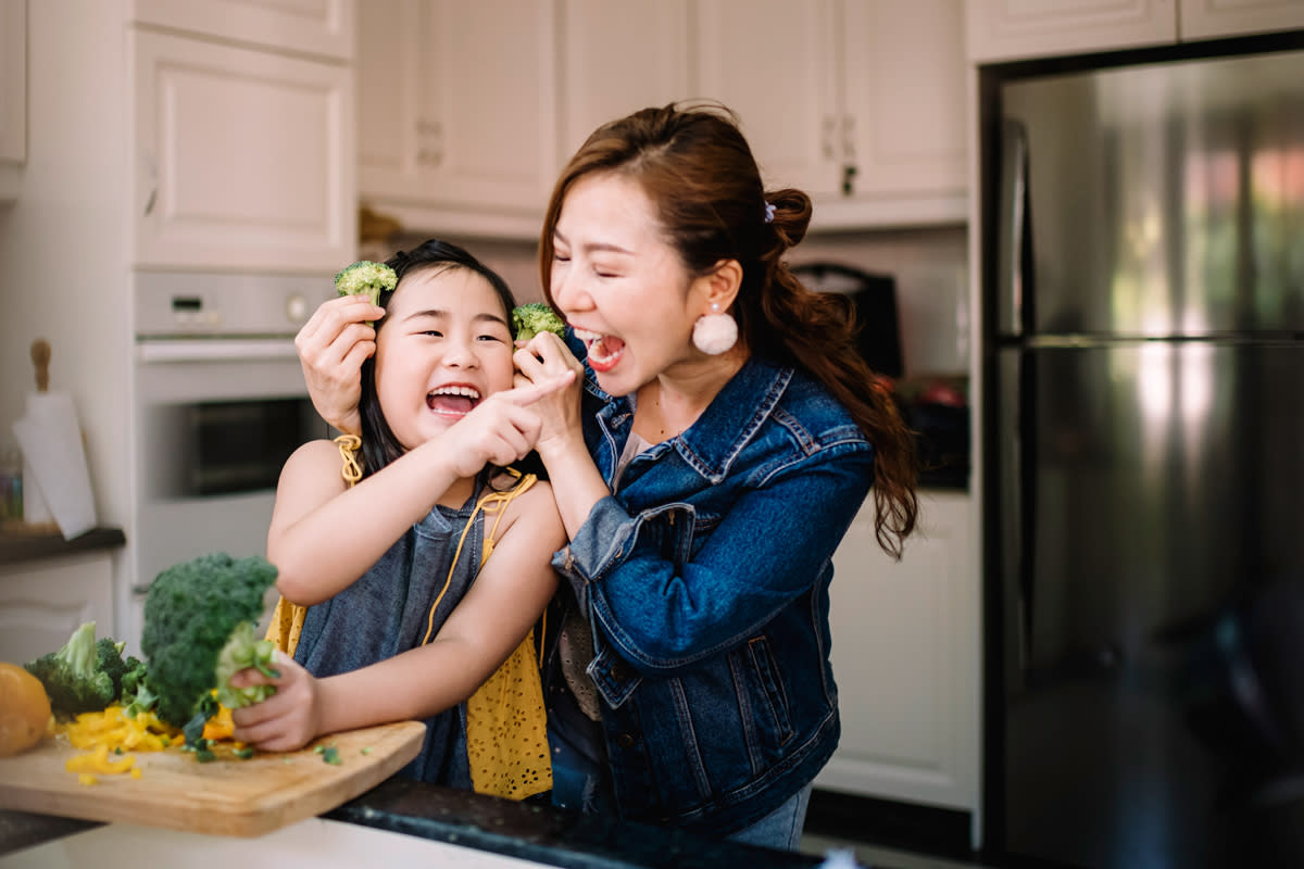 A mother prepares food with her daughter in their kitchen, including broccoli. 