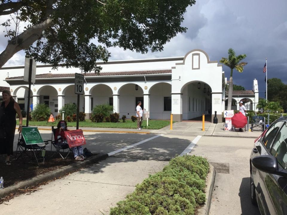 Campaigners wait for voters outside the Orange Blossom Drive library headquarters building as dark clouds loom Tuesday afternoon.