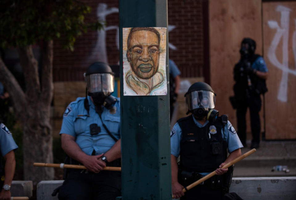 A portrait of George Floyd hangs on a street light pole as police officers stand guard at the Third Police Precinct during a face off with a group of protesters in Minn., Minnesota, May 27, 2020. | Stephen Maturen—Getty Images