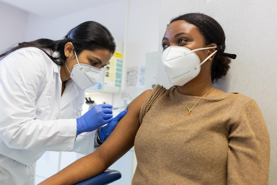 Healthcare professional administering a vaccine to a seated woman in a medical clinic. Both are wearing face masks