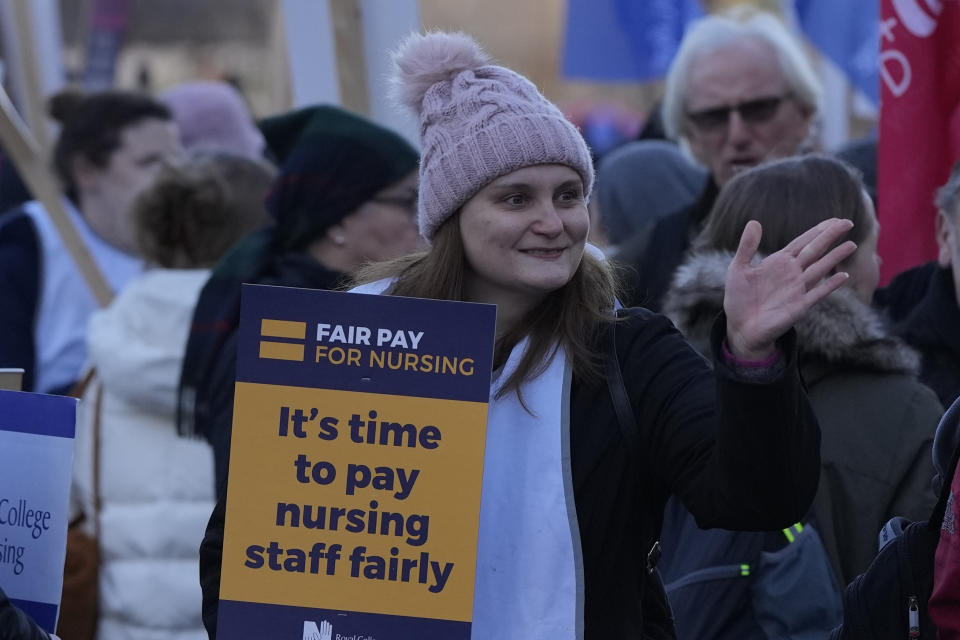 A demonstrator on the picket line holds up placard in support of the nurses pay strike, as she waves to a supporter outside St Thomas's Hospital in London, Tuesday, Dec. 20, 2022. Nurses in England, Wales and Ireland will stage the biggest strike in the history of the Royal College of Nursing (RCN). Up to 100,000 members will walk out at 65 NHS organisations. (AP Photo/Alastair Grant)