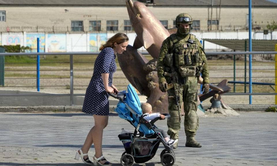 A woman with her child walks past a Russian soldier at an embankment of the Black Sea in Kherson.