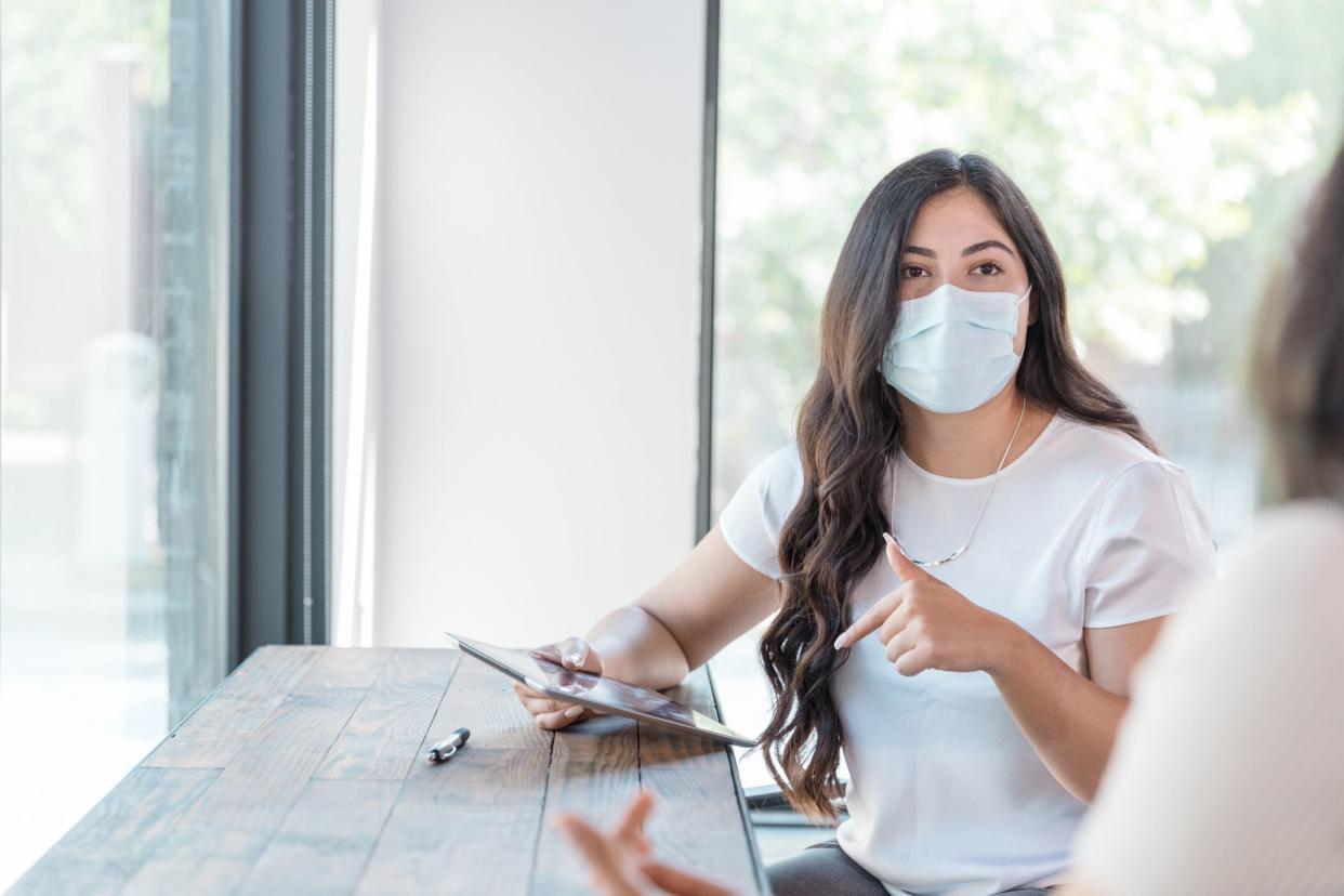 During the coronavirus outbreak, two young adult women wear their protective masks and social distance to meet together. They are gesturing during their conversation.