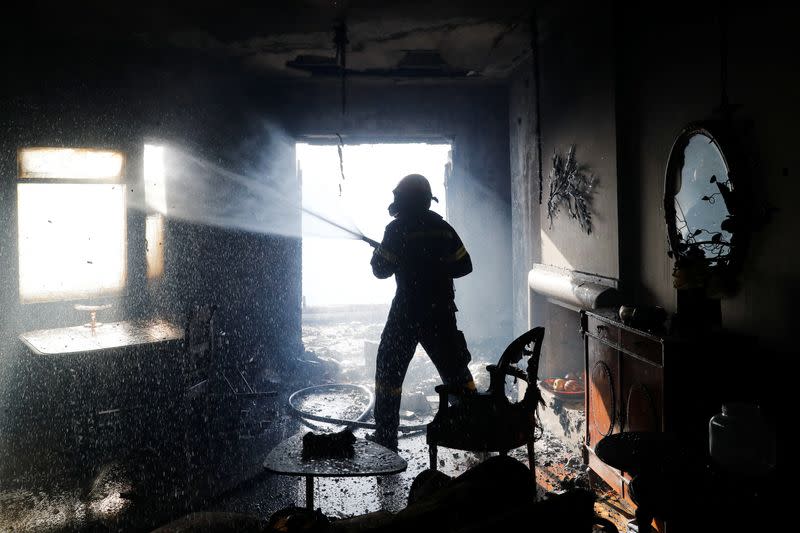 A firefighter sprays water on a damaged house during a wildfire in Voula, south of Athens