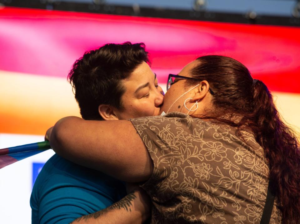 Two women kiss in front of a Pride flag.