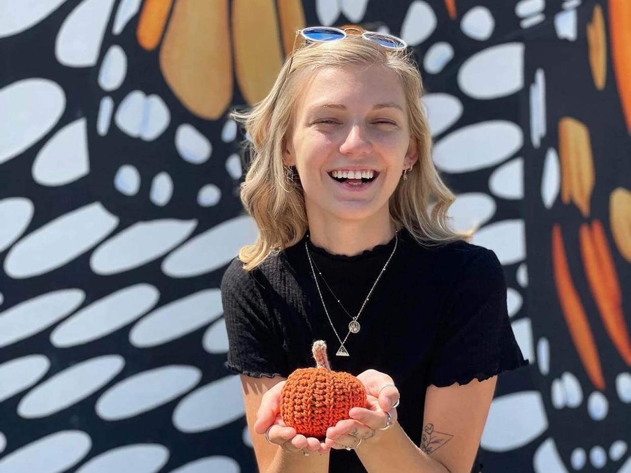 Gabby Petito smiles while holding a small knit pumpkin with both hands.