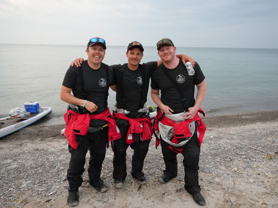 Jeff Guy, Kwin Morris and Joe Lorenz stand on the shores of Lake Ontario in June 2023 after standup paddling from Toronto to the U.S. shoreline and back. The group has paddled across all five Great Lakes to raise awareness about the environmental issues that the lakes face.