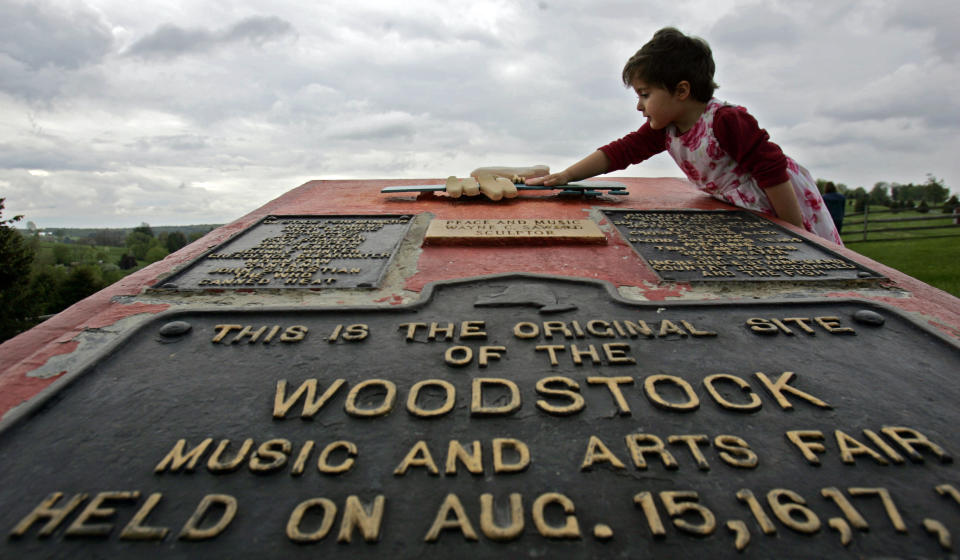 FILE - This May 15, 2008 file photo shows Emma Cenholt, 3, of Trumbull, Conn., playing on a memorial at the site of the Woodstock Music and Arts Fair in Bethel, N.Y. The Woodstock 50 festival is back on after a court on Wednesday, May 15, 2019, rebuffed an ex-investor’s effort to cancel the anniversary extravaganza. But organizers will have to do without some $18 million, at least for now. (AP Photo/Mike Groll, File)