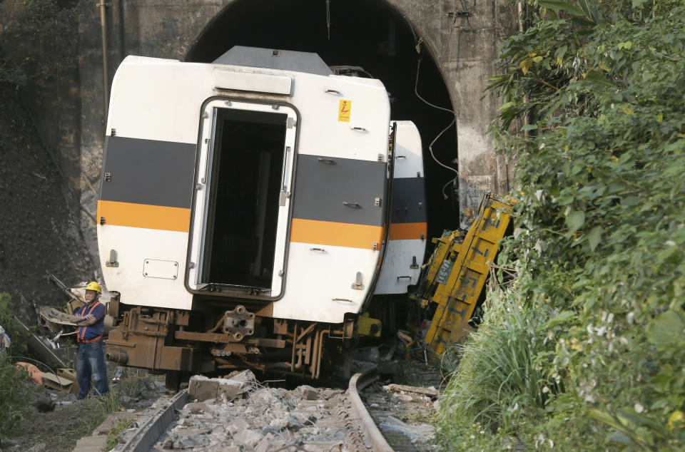 A worker stands in front of the derailed train near Taroko Gorge in Hualien, Taiwan on Saturday, April 3, 2021. The train partially derailed in eastern Taiwan on Friday after colliding with an unmanned vehicle that had rolled down a hill, killing and injuring dozens. (AP Photo/Chiang Ying-ying)