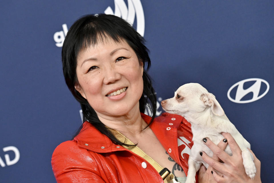 Woman in a red jacket holds a small dog at a celebrity event